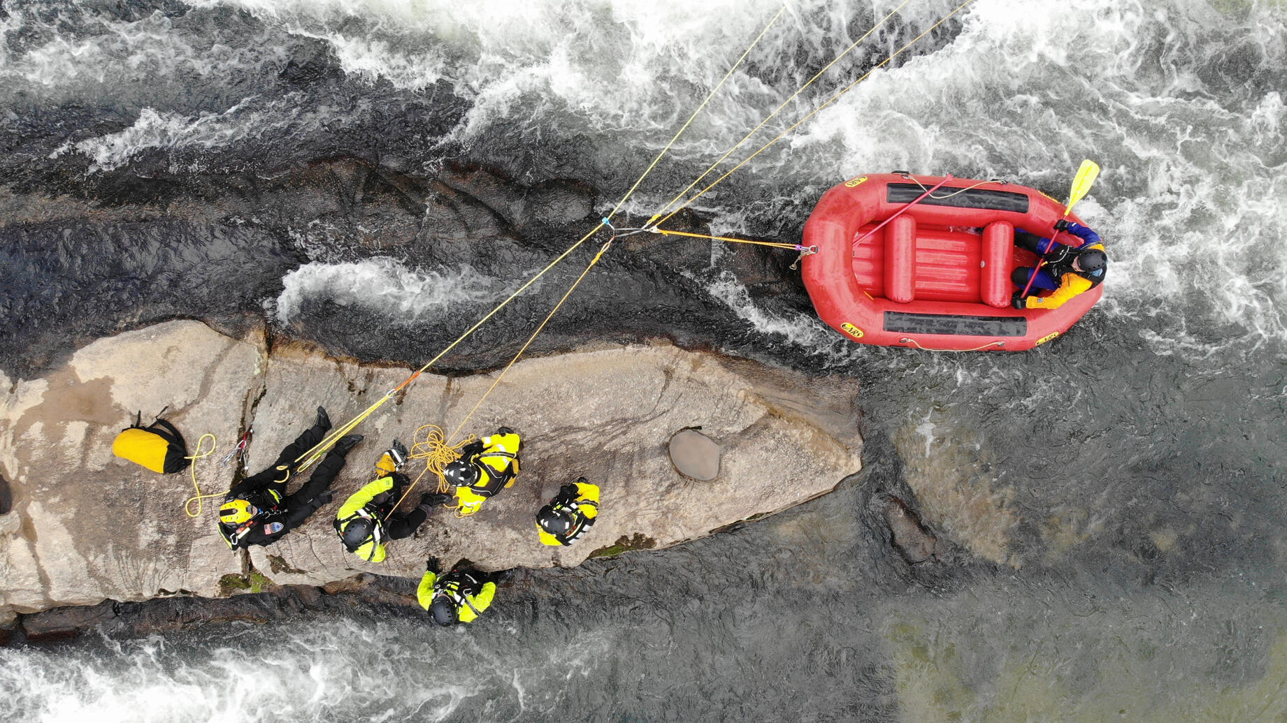 A group of rescuers on a rock working with a rope system to pull a boat through rapids
