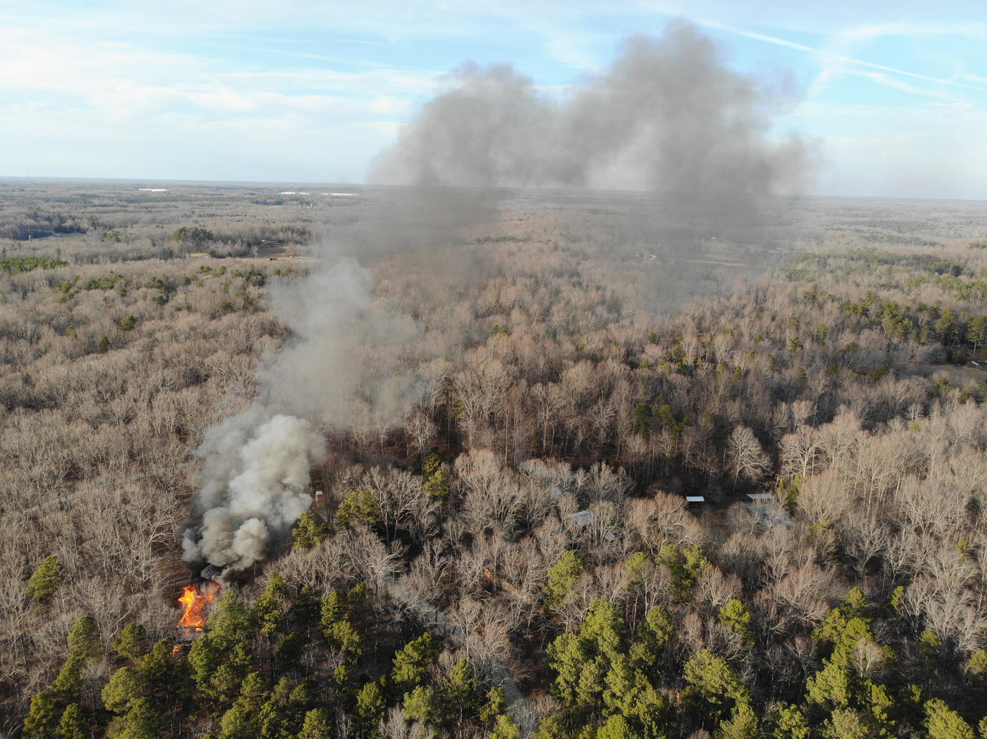 An overhead shot of a house fire in the middle of a large forested area