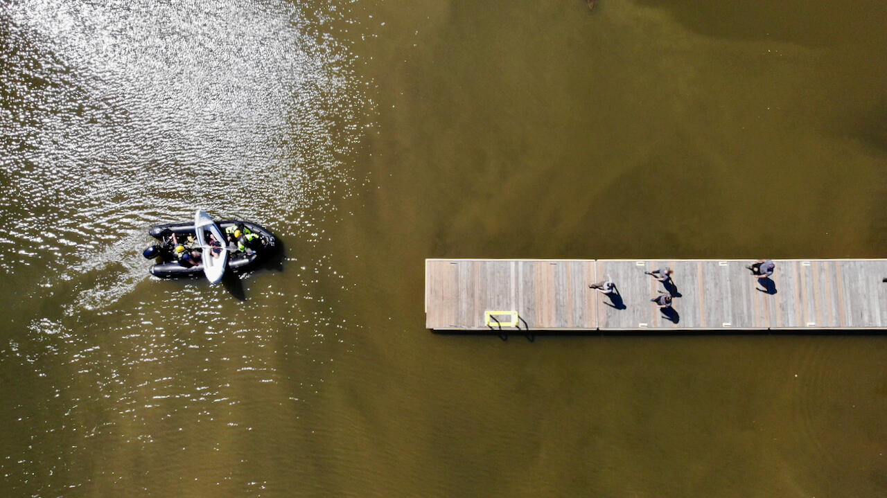 A group of rescuers walking down a dock to greet a rescue boat approaching taking from overhead